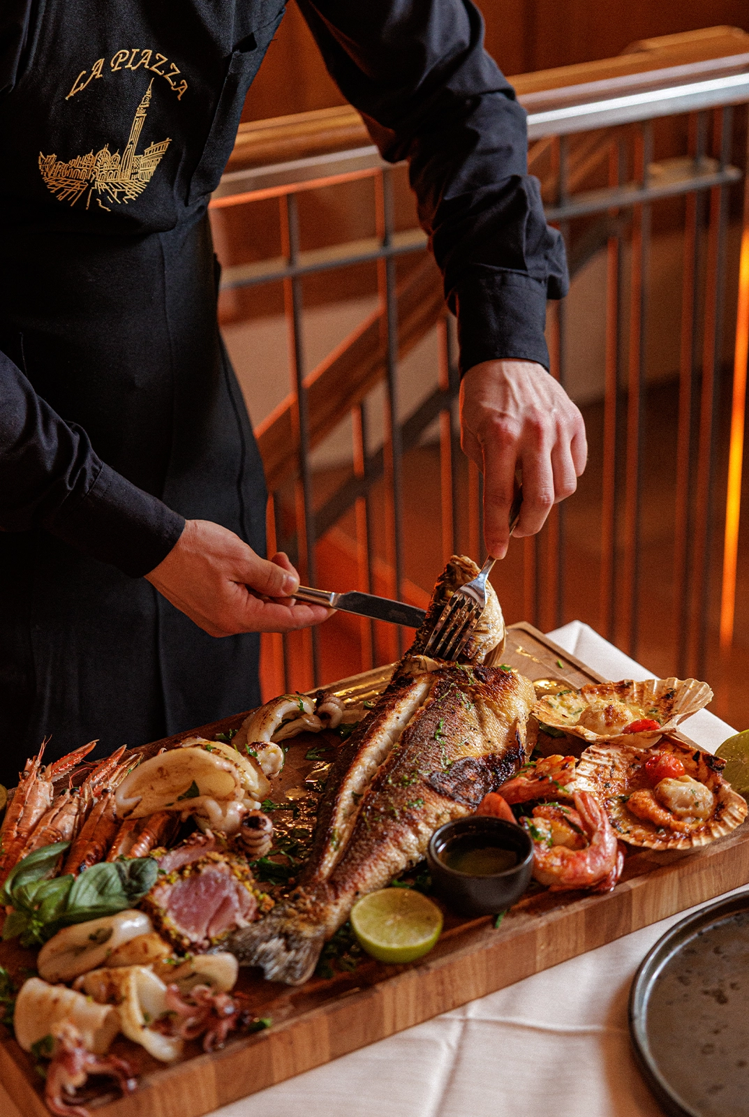 Waiter filleting a whole grilled Adriatic fish at the table, with prawns, squid and scallops, at Ristorante La Piazza near St Mark’s Square, Venice